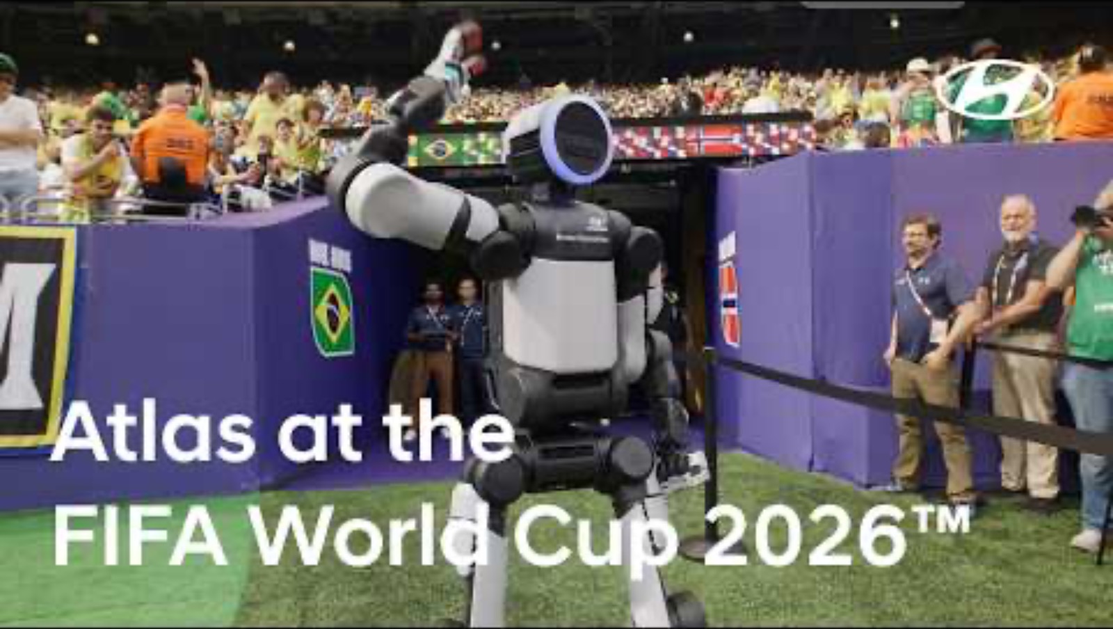 The Atlas humanoid robot raises an arm on the sideline at the FIFA World Cup 2026, crowd and flags behind it