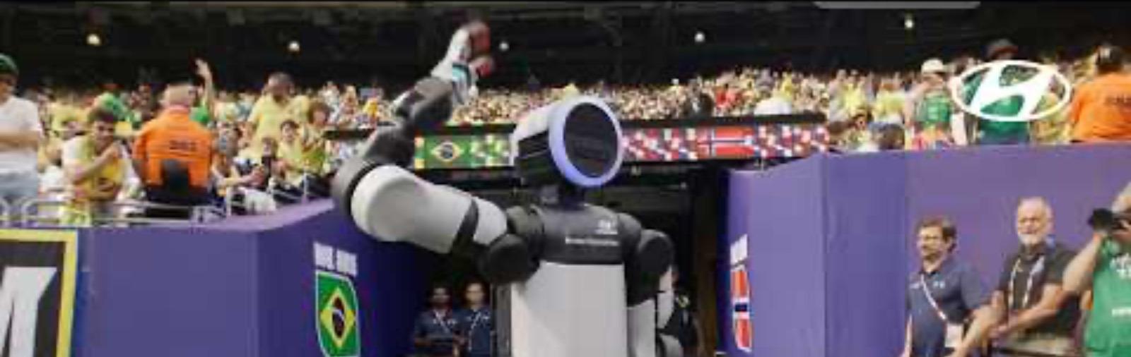 A humanoid robot raises an arm on the sideline of a packed FIFA World Cup stadium, fans and national flags in the background