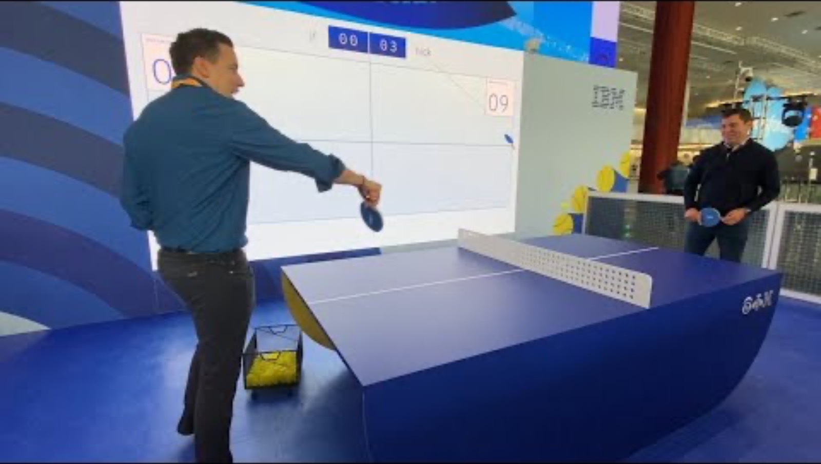 A man rallies against a robotic table-tennis system with a real-time tracking display, referenced in a news story on generative AI commentary
